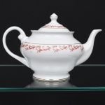 Porcelana Rio Branco/Cia. Brasileira de Vidros, Rio de Janeiro - RJ(Fundada em 1947, ativa até 1967). Elegante bule para chá executado em porcelana nacional da década de 1950/50, executado ao estilo francês do período Luís XV; esmaltagem vítrea na cor branca, decoração em esmalte vermelho-coral, formada por arabescos e ramos vegetalistas estilizados, realçada com filetes em douradura; corpo de perfil balaústre assentado sobre base circular, boca ligeiramente revirada para fora, bico vertedor curvilíneo, alça lateral em voluta, tampa campaniforme encimada por puxador ovoide. Marca da manufatura no verso. Medidas: Alt.: 16,5 x Comp.: 25,5 x Larg.: 16 cm.