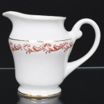 Porcelana Rio Branco/Cia. Brasileira de Vidros, Rio de Janeiro - RJ(Fundada em 1947, ativa até 1967). Elegante leiteira executada em porcelana nacional da década de 1950/50, executado ao estilo francês do período Luís XV; esmaltagem vítrea na cor branca, decoração em esmalte vermelho-coral, formada por arabescos e ramos vegetalistas estilizados, realçada com filetes em douradura; corpo de perfil balaústre assentado sobre base circular, bico vertedor revirado para fora, alça lateral em voluta. Marca da manufatura no verso. Medidas: Alt.: 1,2,5 x Comp.: 15 x Larg.: 9,5 cm.