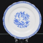 ROSSLAU - ALEMANHA. Exuberante prato de seviço em porcelana alemã, de contorno recortado com aba larga levemente ondulada. Esmaltação branca, decoração apresenta composição em azul padrão china-blau, característica da tradição decorativa centro-europeia inspirada nas porcelanas orientais; aba ornada por friso contínuo em azul com motivos florais estilizados e elementos geométricos, delimitado por filete dourado acompanhando o contorno ondulado da borda, campo central apresenta vinheta decorativa em azul, composta por arranjo floral acompanhado de pequeno elemento ornamental representando ânfora sobre base. Marca na base em azul: CHINA-BLAU / ROSSLAU, indicando manufatura da fábrica Rosslau, Alemanha. Medida: Diam.: 30,5 cm.