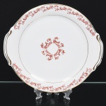 Porcelana Rio Branco/Cia. Brasileira de Vidros, Rio de Janeiro - RJ (Fundada em 1947, ativa até 1967). Elegante Travessa de serviço em porcelana nacional da década de 1950/50;  esmaltagem vítrea na cor branca, formato circular com aba larga e duas alças laterais integradas, decoração em esmalte vermelho-coral, formada por arabescos e ramos vegetalistas estilizados, dispostas ao redor da orla, e radialmente ao centro, realçada com filetes em douradura. Marca da manufatura no verso. Medidas: Diam.: 29,5 cm.