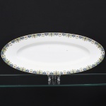 Andrieux & Co. Limoges, Limoges - França. Travessa oval executada em porcelana francesa, da região de Limoges; esmaltação branca, centro ligeiramene rebaixado, borda decorada com friso policromo composto por cartelas geométricas azuis e verdes alternadas, intercaladas por pequenos medalhões com borboletas, além de motivos florais estilizados e grinaldas vegetalistas delicadas dispostas ao longo da aba. Marca da manufatura no verso. Medidas: Comp.: 49 x Larg.: 20 cm.
