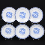 ROSSLAU - ALEMANHA. Exuberante conjunto de pratos rasos em porcelana alemã, de contorno recortado com aba larga levemente ondulada. Esmaltação branca, decoração apresenta composição em azul padrão china-blau, característica da tradição decorativa centro-europeia inspirada nas porcelanas orientais; aba ornada por friso contínuo em azul com motivos florais estilizados e elementos geométricos, delimitado por filete dourado acompanhando o contorno ondulado da borda, campo central apresenta vinheta decorativa em azul, composta por padrão de flores, ânfora e elementos arquitetônicos. Marca no verso em azul: CHINA-BLAU / ROSSLAU, indicando manufatura da fábrica Rosslau, Alemanha. Composto de seis(06) unidades. Medida: Diam.: 24 cm.