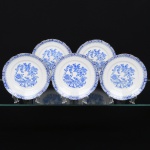 ROSSLAU - ALEMANHA. Exuberante conjunto de pratos para sobremesa em porcelana alemã, de contorno recortado com aba larga levemente ondulada. Esmaltação branca, decoração apresenta composição em azul padrão china-blau, característica da tradição decorativa centro-europeia inspirada nas porcelanas orientais; aba ornada por friso contínuo em azul com motivos florais estilizados e elementos geométricos, delimitado por filete dourado acompanhando o contorno ondulado da borda, campo central apresenta vinheta decorativa em azul, composta por padrão de flores, ânfora e elementos arquitetônicos. Marca no verso em azul: CHINA-BLAU / ROSSLAU, indicando manufatura da fábrica Rosslau, Alemanha. Composto de cinco(05) unidades. Medida: Diam.: 19,5 cm.
