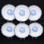 ROSSLAU - ALEMANHA. Exuberante conjunto de pratos fundos em porcelana alemã, de contorno recortado com aba larga levemente ondulada. Esmaltação branca, decoração apresenta composição em azul padrão china-blau, característica da tradição decorativa centro-europeia inspirada nas porcelanas orientais; aba ornada por friso contínuo em azul com motivos florais estilizados e elementos geométricos, delimitado por filete dourado acompanhando o contorno ondulado da borda, campo central apresenta vinheta decorativa em azul, composta por padrão de flores, ânfora e elementos arquitetônicos. Marca no verso em azul: CHINA-BLAU / ROSSLAU, indicando manufatura da fábrica Rosslau, Alemanha. Composto de cinco(05) unidades. Medida: Diam.: 24 cm.