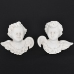 Par de esculturas decorativas em porcelana de biscuit, tonalidade branca, representando querubins alados modelados em busto, apresentam rosto infantil de feições suaves, cabelos ondulados e asas abertas, com tratamento escultórico em relevo que destaca os cachos do cabelo, as penas das asas e o drapeado estilizado na base do busto, parte posterior dotado de orifício circular para fixação em parede. Medidas: Alt.: 11,5 x Comp.: 12,5 x Larg.: 6 cm.