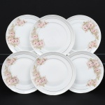 Porcelana Real, Mauá - SP(Fundada em 1943 por Fritz Erwin Schmidt). Conjunto de pratos rasos em porcelana nacional, esmaltação na cor branca, decoração com arranjos florais em tonalidades suaves de rosa, acompanhadas por folhas em verde claro, dispostos lateralmente na aba, complementado por filetes dourados finos aplicados próximos à borda e na linha interna da aba. Marca da manufatura no verso. Composto de seis(06) unidades. Medida: Diam.: