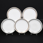 Porcellana Mauá, Mauá - SP(Fundada em 1937 por Fritz Erwin Schmidt / ativa até 1968). Elegante conjunto de pratos rasos em porcelana nacional da década de 1950/60; esmaltação branca, orla circundada por faixa com padrão de meandro grego, entre frisos em douradura contornando a borda e o centro. Marca da manufatura no verso. Composto de cinco(05) unidades. Medida: Diam.: 24 cm.