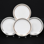 Porcellana Mauá, Mauá - SP(Fundada em 1937 por Fritz Erwin Schmidt / ativa até 1968). Elegante conjunto de pratos rasos em porcelana nacional da década de 1950/60; esmaltação branca, orla circundada por faixa com padrão de meandro grego, entre frisos em douradura contornando a borda e o centro. Marca da manufatura no verso. Composto de quatro(04) unidades. Medida: Diam.: 24 cm.