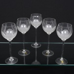 Conjunto taças de pé alto, para vinho branco, executadas em fino cristal europeu, diáfano e incolor; bojo globular, fundo preenchido e talhado com flor acetinada, fuste tubular alongado sobre base circular. Composto de cinco(05) unidades. Medidas: Alt.: 25 x Diam.: 8 cm.