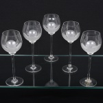 Conjunto taças de pé alto, para vinho tinto, executadas em fino cristal europeu, diáfano e incolor; bojo globular, fundo preenchido e talhado com flor acetinada, fuste tubular alongado sobre base circular. Composto de cinco(05) unidades. Medidas: Alt.: 18,5 x Diam.: 7 cm.