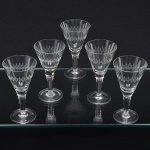 Elegante conjunto de taças de pé alto, para licor, em cristal, diáfano e incolor, bojo obcônico lapidado com sucessão de navetes dispostas horizontalmente, fuste cilíndrico sobre base circular. Composto de seis(06) unidades. Medidas: Alt.: x Diam.: