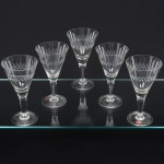 Elegante conjunto de taças de pé alto, para ,em cristal, diáfano e incolor; bojo obcônico lapidado com sucessão de navetes dispostas horizontalmente, fuste cilíndrico sobre base circular. Composto de cinco(05) unidades. Medidas: Alt.: x Diam.: