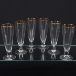 Conjunto composto por seis(06) taças tipo flûte em cristal incolor, apresentando bojo alto e estreito de perfil cônico alongado, apoiado sobre haste cilíndrica curta e base circular plana, borda circundada por friso em douradura. Medidas: Alt.: x Diam.: