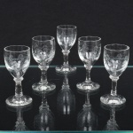 Conjunto composto por cinco(05) cálices em cristal incolor, apresentando bojo ovóide levemente afunilado, apoiado sobre haste curta cilíndrica com anel central e base circular plana, gravado com composição de ramos vegetalistas com folhas e frutos estilizados, formando composição contínua. Medidas: Alt.: x Diam.: