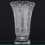 Exuberante vaso executado em cristal europeu, diáfano e incolor, corpo obcônico alongado, com abertura ampla, borda movimentada e recortada. Decoração executada por lapidação geométrica profunda, composta por painéis verticais alternando motivos de estrelas radiadas, rosetas, losangos e reticulados, delimitados por filetes verticais facetados, base espessa escalonada, de secção octogonal, com lapidação radial inferior formando estrela de múltiplas pontas, provavelmente produção centro-europeia, dentro da tradição do cristal da Boêmia. Apresenta pequena quebradura numa das pontas da borda. Medidas: Alt.: 31 x Diam.: 20 cm.