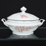 Porcelana Real, Mauá - SP(Fundada em 1943 por Fritz Erwin Schmidt). Sopeira em porcelana nacional, esmaltação na cor branca, decoração com arranjos florais em tonalidades suaves de rosa, acompanhadas por folhas em verde claro, dispostos lateralmente no bojo e na tampa, complementado por filetes dourados finos aplicados próximos à borda; tampa abaulada encimada por puxador com feitio de fruto, alças laterais reviradas para cima. Marca da manufatura no verso. Medidas: Alt.: x Comp.: x Larg.: