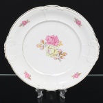 Porcelana Real, Mauá - SP(Fundada em 1943 por Fritz Erwin Schmidt). Travessa executada em porcelana nacional da década 1950, esmaltagem vítrea na cor branca, formato oval com aba larga e bordas recortadas em relevo, apoiada sobre base plana com pequeno anel de apoio. moldada com delicado relevo ornamental nas extremidades da aba, decorada com padrão floral em estampagem policromada, predominando as tonalidades rosa e amarelo, acompanhada por folhas e folhagens em tona de verde e ocre, aplicado no centro e replicado em pequenos buquês ao redor da orla, borda contornada por friso em douradura. Marca da manufatura no verso. Medida: 