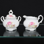 Porcelana Real, Mauá - SP(Fundada em 1943 por Fritz Erwin Schmidt). Um(01) açucareiro e uma(01) cremeira em porcelana nacional, esmaltação branca modelada com frisos verticais; corpo bojudo decorado com composição floral em estampagem policromada, predominando as tonalidades rosa, amarelo e ocre, bordas e contornos realçados com friso em douradura. Marca da manufatura ao fundo. Medidas: