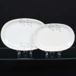 Porcelana Renner, Porto Alegre - RS(Fundada em 1937). Duas(02) travessas ovais em porcelana nacional, esmaltagem vítrea na cor branca, decorado com flores estilizadas em estampagem policromada, orla delimitada por friso em douradura. Medidas: Comp.: x Larg.: ; Comp.: x Larg.: