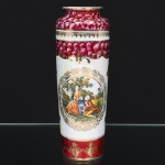 Vaso em porcelana nacional da década de 1950/60, corpo cilíndrico alongado, com borda levemente evertida. Decoração em esmaltação policroma e douração, apresentando cena galante de inspiração rococó em reserva central, circundada por frisos ornamentais. Faixas superiores e inferiores em tom rubi marmorizado com detalhes em ouro. Verso com motivos florais estilizados esparsos. Marca da manufatura ao fundo. Medidas:
