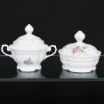 Porcelana Real, Mauá - SP(Fundada em 1943 por Fritz Erwin Schmidt). Um(01) açucareiro e uma(01) manteigueira em porcelana nacional, esmaltação branca modelada com gomos em relevo; corpo bojudo decorado com composição floral em estampagem policromada, predominando as tonalidades rosa e verde, bordas e contornos realçados com friso em douradura, alças laterais em voluta e pega da tampa ovoide. Marca da manufatura ao fundo. Medidas: