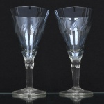 Duas(02) taças de pé alto em cristal para vinho tinto, diáfano, levemente azulada, bojo obcônico talhado com folhagens estilizadas dispostas em faixas horizontal, fuste tubular de topo facetado, base circular. Medidas: Alt.: 16 x Diam.: 8,5 cm. Uma com discreto bicado na borda da boca.