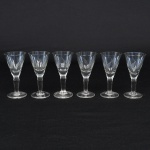 Conjunto de taças de pé alto em cristal para licor, diáfano, levemente azulada, bojo obcônico talhado com folhagens estilizadas dispostas em faixas horizontal, fuste tubular de topo facetado, base circular. Composto de seis(06) unidades. Medidas: Alt.: 10,5 x Diam.: 5 cm.