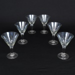 Conjunto de taças de pé alto em cristal para champanhe, diáfano, levemente azulada, bojo obcônico talhado com folhagens estilizadas dispostas em faixas horizontal, fuste tubular de topo facetado, base circular. Composto de seis(06) unidades. Medidas: Alt.: 14,5 x Diam.: 10 cm.