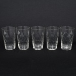 Conjunto de copos em meio cristal, diáfano e incolor, bojo cilíndrico decorado com lapidação geométrica em padrão losangular e folhagens estilizadas, distribuídas na porção média. Composto de cinco(05) unidades. Medidas: