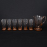 Elegante conjunto em meio cristal, translúcido, tonalidade marsala; composto de uma(01) jarra e cinco(05) copos de formato obcônico, talhados com composição de losangos verticais entrecruzados e nervuras ascendentes, formando desenho repetitivo em faixas, sob colar de janelas circulares facetadas; Jarra com bico vertedor revirado para fora, alça lateral curvada, base circular com fundo preenchido por estrela raiada. Medidas: Jarra: Alt.: 21,5 x Comp.: 20 x Larg.: 15 cm. Copos: Alt.: 16,5 x Diam.: 8 cm.