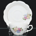 Porcelana Renner, Porto Alegre - RS(Fundada em 1937). Xícara para chá em porcelana nacional, esmaltação branca, bojo hemisférico com alça lateral em voluta, decorado com arranjo floral em estampagem policromada, centralizada por friso em douradura, borda do pires recortada em ondulações. Marca da manufatura ao fundo. Medidas: Xícara: Alt.: 5,5 x Comp.: 12 x Larg.: 9,5 cm. Pires: Diam.: 15,5 cm.