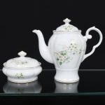 Porcelana Real, Mauá - SP(Fundada em 1943 por Fritz Erwin Schmidt). Um(01) bule para café e uma(01) manteigueira em porcelana nacional, esmaltação branca modelada com gomos em relevo; bojo decorado com composição floral em estampagem policromada, predominando as tonalidades verde, amarelo e castanho, bordas e contornos realçados com friso em douradura; alça lateral em voluta, bico vertedor curvilíneo, tampa ligeiramente abaulada sob pega com feitio de disco.  Marca da manufatura ao fundo. Medidas: