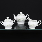 Porcelana Real, Mauá - SP(Fundada em 1943 por Fritz Erwin Schmidt). Um(01) bule para chá, um(01) açucareiro e uma(01) leiteira em porcelana nacional, esmaltação branca modelada com gomos em relevo; bojo decorado com composição floral em estampagem policromada, predominando as tonalidades verde, amarelo e castanho, bordas e contornos realçados com friso em douradura; alças laterais em voluta, bico vertedor ondulado e curvilíneo, tampa ligeiramente abaulada sob pega com feitio de disco.  Marca da manufatura ao fundo. Medidas:
