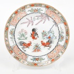 Prato de coleção em porcelana chinesa, esmaltação branca, decoração em esmaltes policromos no estilo de exportação chinesa de inspiração famille rose, com repertório decorativo associado ao chamado Imari chinês, evocando modelos do século XVIII (dinastia Qing). Medalhão central com representação de galos entre elementos fitomorfos, incluindo rochedos e ramos floridos. Aba ornada por reservas alternadas com motivos geométricos de padrão meândrico e elementos florais estilizados, delimitadas por filetes. Verso com marca em caracteres chineses em vermelho sob o vidrado. Medida: Diam.: