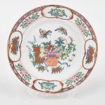 Prato de coleção em porcelana chinesa, esmaltação branca, decoração em esmaltes policromos no estilo de exportação chinesa de inspiração famille rose, com repertório decorativo derivado de modelos Qing do século XVIII. Medalhão central com arranjo floral em vaso, ladeado por insetos alados. Aba com reservas ovais contendo composições florais, intercaladas por frisos com motivos fitomorfos e elementos geométricos estilizados, delimitados por filetes de tonalide vermelho-ferro(rouge de fer). Verso com marca impressa em laranja sob o vidrado, inscrição Hand Painted Decoration / Made in China acompanhada de caracteres chineses. Medidas: Diam.: