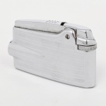 Isqueiro em metal cromado, corpo retangular com linhas horizontais gravadas e elementos aerodinâmicos nas extremidades; mecanismo com roda lateral e tampa articulada. Marca da manufatura ao fundo. Não foi testado, sem garantias de funcionamento. Medidas: