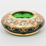 Cinzeiro de mesa em vidro veneziano, tonalidade verde esmeralda, formato elipsoide, borda com aberturas recortadas em arcos para apoio, decoração esmaltada e douração executada por pintura a esmalte e generosa douração. Medidas: