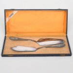 EBERLE. Duas(02) espátulas confeccionadas em metal prateado, cabo de ponta oval, decorado com friso relevado, volutas e concha. Marca da manufatura no verso. Acondicionadas em estojo original. Estado conforme fotografias. Medidas: