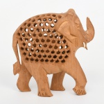 Escultura em madeira entalhada, produção artesanal, representando elefante em posição de marcha, executada em bloco único, com corpo vazado em padrão geométrico perfurado, cabeça com tromba elevada, presas aparentes e detalhes incisos nas patas. Acabamento natural, sem policromia, com evidência de entalhe manual. Medidas: