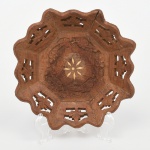 Fruteira executada em madeira, formato octogonal, com bordo recortado em lobulações sucessivas e segmentos vazados por recorte geométrico. Corpo de perfil baixo e côncavo, com bojo facetado correspondente aos lados do octógono. Campo central em reserva circular rebaixada, ornamentado por marchetaria radial em motivo estelar; cercadura interna com entalhe em baixo-relevo de composição fitomorfa. Execução manual, com marcas de ferramenta visíveis. Estado conforme fotografias, apresenta trincas e perdas. Medidas: