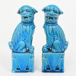 Elegante par de esculturas representando cães de fó, executadas em cerâmica cobertas com esmaltagem vítrea na tonalidade azul turquesa, dotados de rica ornamentação modelada em relevo. Apresentam-se com postura tradicional, bocas abertas com a língua para fora, um com uma das patas apoiadas sobre esfera vazada, e outro em cima de um filhote; ambos assentados sobre base alta de formato retangular. Medidas: Alt.: 12 x Comp.: 5 x Larg.: 3,5 cm.