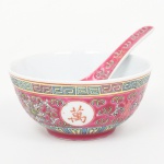 Tigela em porcelana chinesa, corpo hemisférico com pé anelar, decoração em esmaltação policroma com fundo rosa, frisos geométricos contínuos, reservas circulares com caracteres chineses e elementos florais estilizados; colher com decoração correspondente. Base com marca em vermelho MADE IN CHINA. Medidas: