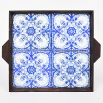 Bandeja de formato retangular, em madeira, com abas laterais integradas e borda elevada. Fundo composto por quatro azulejos cerâmicos justapostos, decorados em monocromia azul sobre fundo branco, com composição simétrica de caráter vegetalista, centrada em elemento floral estilizado, circundado por volutas e motivos fitomorfos. Medidas: