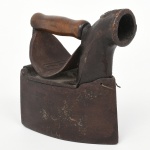 Ferro de engomar a carvão, confeccionado em ferro fundido, com empunhadura em madeira. Corpo maciço com base plana e reservatório interno para carvão; tampa superior articulada por eixo lateral, com abertura para abastecimento; bocal frontal tubular para ventilação e exaustão de gases; pega superior em madeira torneada fixada por suportes metálicos; elemento central curvo com inscrição em relevo BUGRE. Construção por fundição e montagem com articulações mecânicas. Estado conforme fotografias. Medidas: