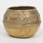 Vaso em metal amarelo, corpo globular com borda espessada, superfície decorada por incisão linear contínua e aplicação de elementos em relevo com motivos florais e geométricos, faixa superior com friso repetitivo e símbolos estilizados. Medidas: