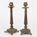 Par de castiçais em metal fundido, com fuste de seção facetada e decoração em relevo longitudinal, assentados sobre base quadrilobada com pés recortados, ornamentada com motivos fitomorfos em relevo. Bobeche sob o bocal e porta-vela cilíndrico na extremidade superior. Superfície com vestígios de douração e pátina de oxidação. Estado conforme fotografias. Medidas: 