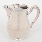 WOLFF. Jarra confeccionada em metal espessurado á prata, bojo de perfil balaústre assentado sobre base circular, bico vertedor revirado para fora, boca dotada de barra vazada retentora de gelo, alça lateral em voluta recoberta por folhas de acanto em relevo. Marca da manufatura ao fundo. Medidas: