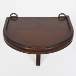 Suporte de parede em madeira, de formato semicircular, com tampo plano dotado de borda elevada e dois olhais metálicos para fixação. Corpo constituído por travessa posterior curva e elemento de sustentação frontal recortado, formando estrutura em balanço. Medidas: Alt.: x Comp.: x Larg.: