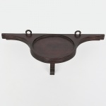 Suporte de parede em madeira, de formato semicircular, com tampo plano dotado de borda elevada e dois olhais metálicos para fixação. Corpo constituído por travessa posterior curva e elemento de sustentação frontal recortado, formando estrutura em balanço. Medidas: Alt.: x Comp.: x Larg.: