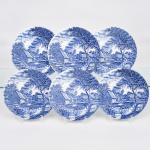 Johnson Brothers, Staffordshire - Inglaterra(Fundada em 1883). Belíssimo conjunto de pratos rasos executado em faiança inglesa, padrão Watermill. Decoração monocromática em azul sob esmalte, representando paisagem rural com moinho hidráulico, executada por estampagem. A composição mostra edifício de moinho com roda dágua em funcionamento, pequeno dique e queda d'água, acompanhados por casas campestres, árvores frondosas, figuras humanas em ambiente bucólico e céu anuviado ao fundo; orla modelada com delicado movimento ondulado, borda recortada com arcos em repetição. Marca da manufatura no verso. Composto de seis(06) unidades. Medida: Diam.: 25 cm.